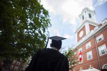 Graduate student with mortar board looking up at a brick building with white trim on campus.